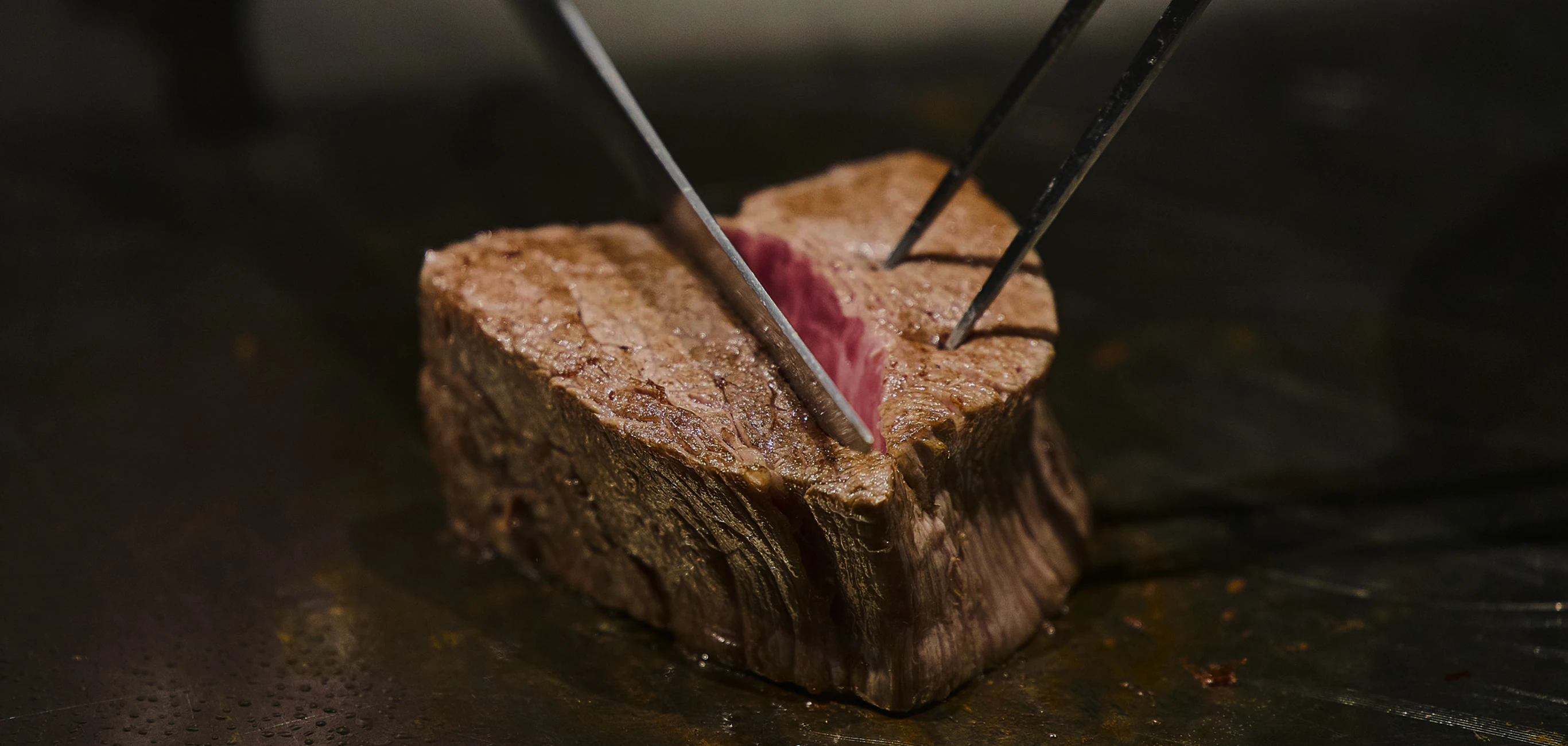 鉄板の上で焼き上げたステーキをカットする様子
