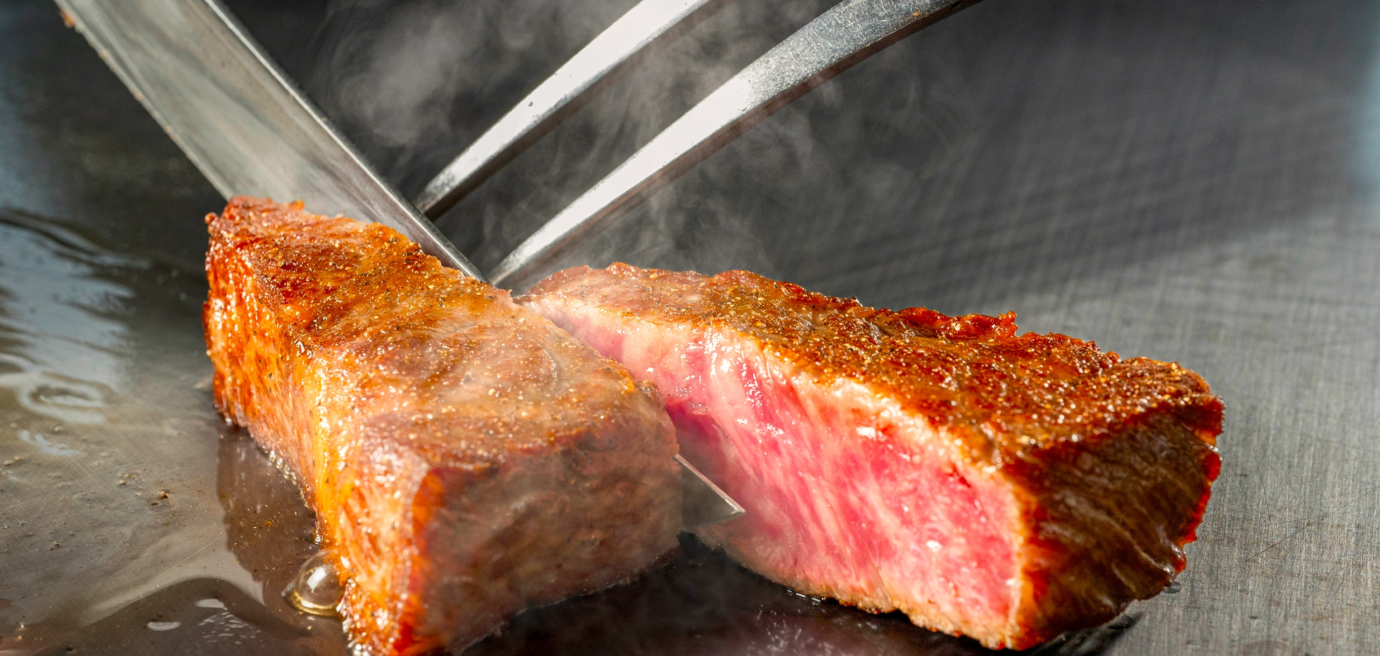 鉄板の上で焼き上げたステーキをカットする様子